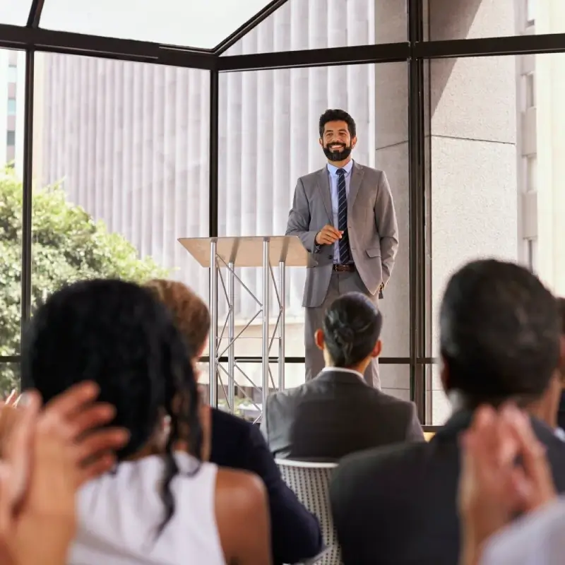 A group of people sitting and applauding a speaker who is on a podium