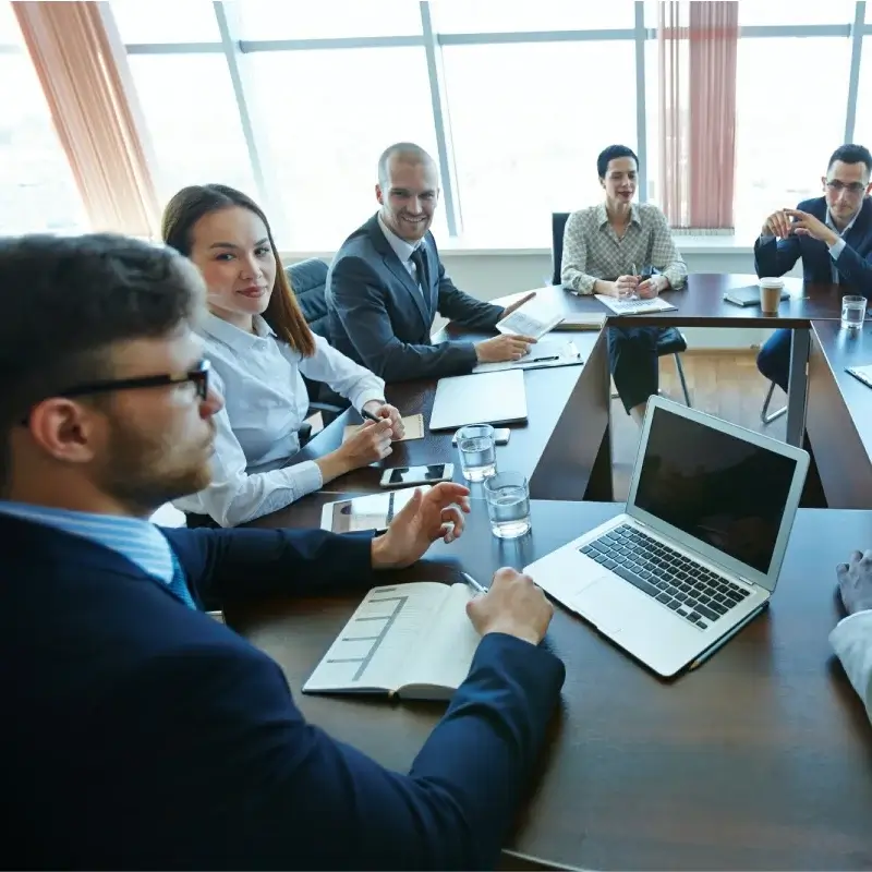 A group of businesspeople gathered in an office with a square table