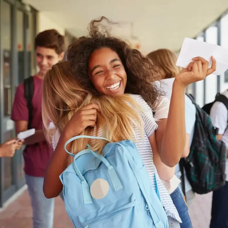 Two female students hugging each other happy for passing an exam