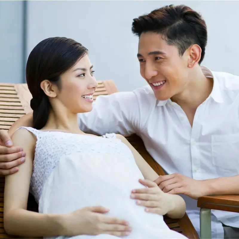 A pregnant woman lying down with her husband embracing her both happy