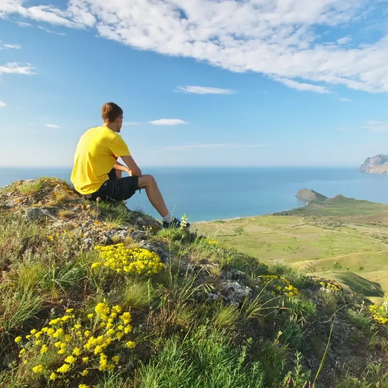 Thoughtful man sitting on a mountain with the sea in the distance