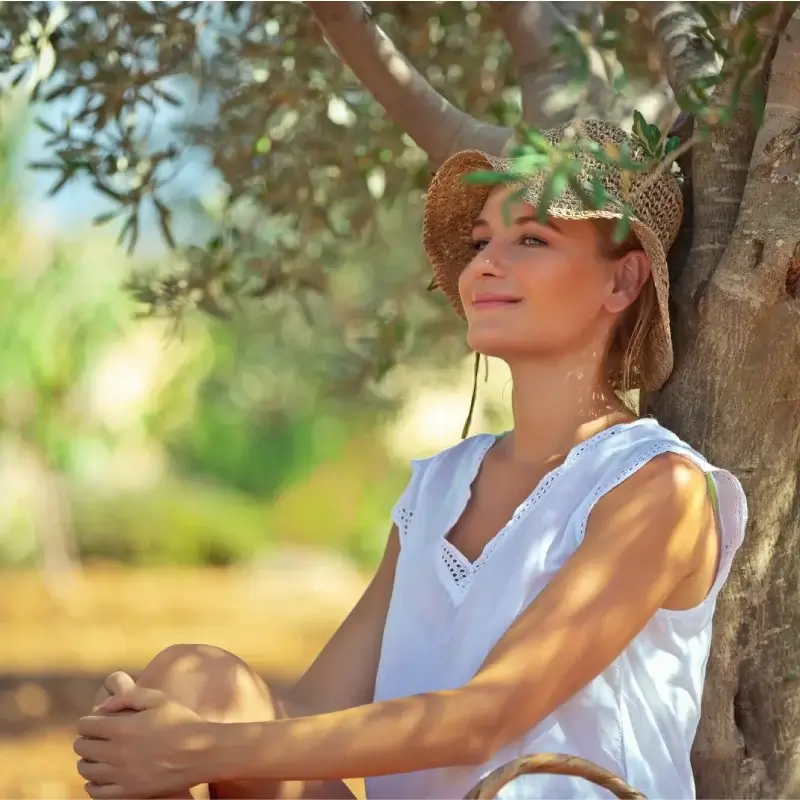 Happy woman with a straw hat sitting under an olive tree